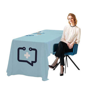 Woman sitting on a chair next to a table with a light blue tablecloth featuring a logo.
